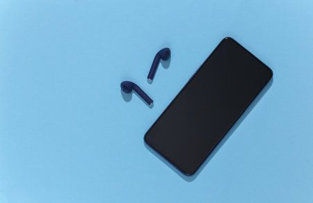 Smartphone and classic blue color true wireless headphones or earbuds on bright blue background. top viewの写真素材