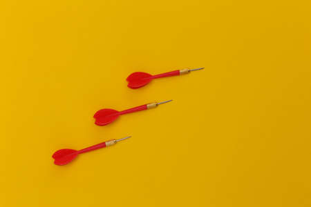 Three red plastic darts with metal tip on yellow background. top view. flat lay