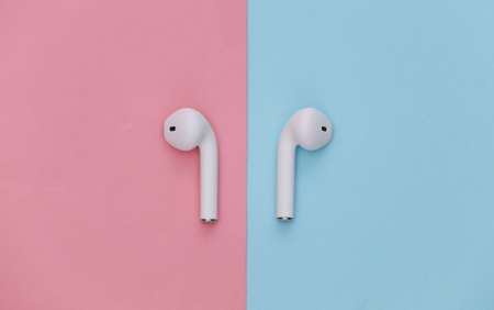 Modern wireless earphones on pink blue pastel background. top view. flat layの写真素材