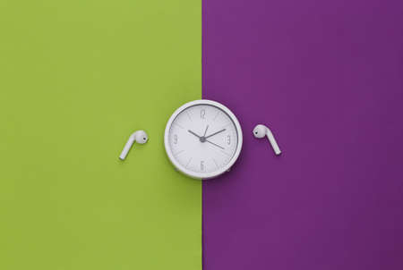 White clock and wireless earphones on a purple-green background. top viewの写真素材