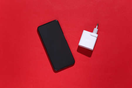Smartphone and charger adapter on red bright background with deep shadow. top view. flat lay....