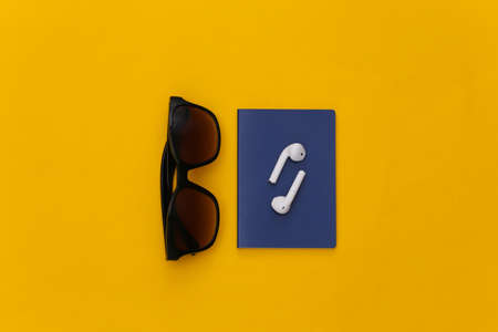 Passport and wireless earphones, sunglasses on a yellow background, travel concept. top viewの写真素材