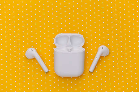 White wireless earphones with charging case on yellow dotted background. top view. flat lay