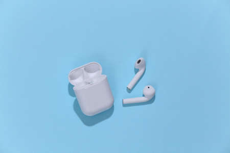 White true wireless headphones or earbuds with charging case on bright blue background. top view