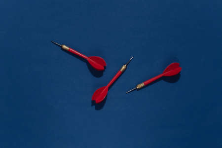 Three red plastic darts with metal tip on classic blue bright background with deep shadow. top view. flat layの写真素材