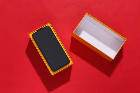 New smartphone in a packing box on red bright background with deep shadow. top view. flat layの写真素材