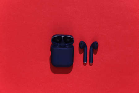 True wireless headphones or earbuds with charging case on bright red background. top view
