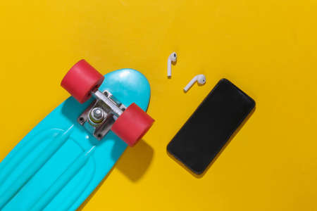 Cruiser board, smartphone and wireless headphones on a bright yellow background. Youth accessories,...