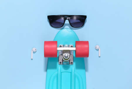 Cruiser board and wireless headphones, sunglasses on a bright blue background. Youth accessories, hipster outfit. top view. flat layの写真素材