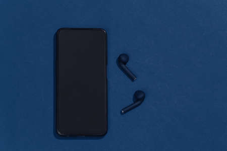 Smartphone and true wireless headphones or earbuds on clasic blue background. top viewの写真素材