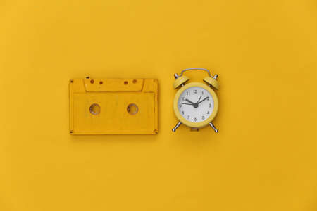 Mini alarm clock and retro audio cassette on a yellow background. top view