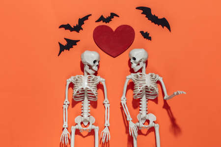 Two Skeletons, bats and red decorative heart on a bright orange background. Valentine's day or...