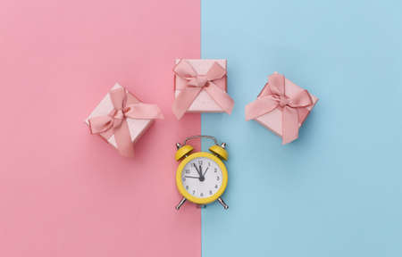 Mini alarm clock and gift box on pink blue pastel background. top view. minimalism