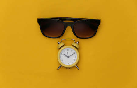 Mini alarm clock and sunglasses on a yellow background. summer holiday time. top view