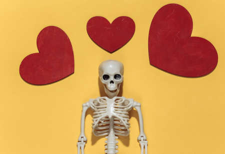 Skeleton and red decorative hearts on a bright yellow background. Valentine's day or halloween theme. top view. flat layの写真素材