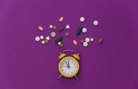 Insomnia. Mini alarm clock and pills on a purple background. top view.の写真素材