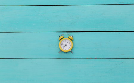 Yellow retro alarm clock on blue wooden background. top view.