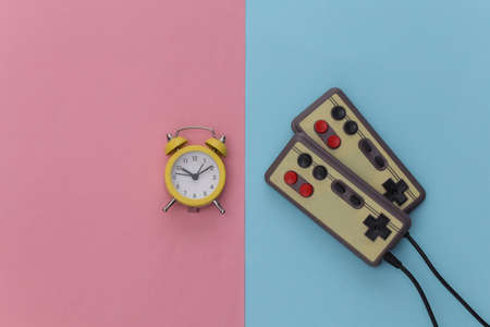 Mini alarm clock and retro joysticks on pink blue pastel background. Time to play video games. 80s. top viewの写真素材