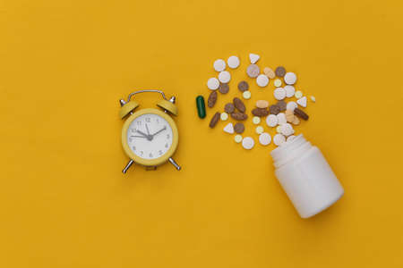 Insomnia. Mini alarm clock and bottle pills on yellow background. top view.の写真素材