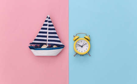 Mini alarm clock and mini sailboat on pink blue pastel background. Time to travel. top viewの写真素材