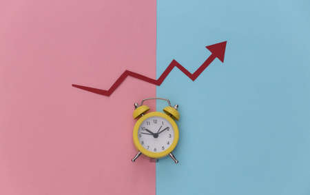 Mini alarm clock and red growth arrow on blue pink pastel background. top viewの写真素材