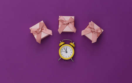 Mini alarm clock and gift boxes on a purple background. top view. minimalism