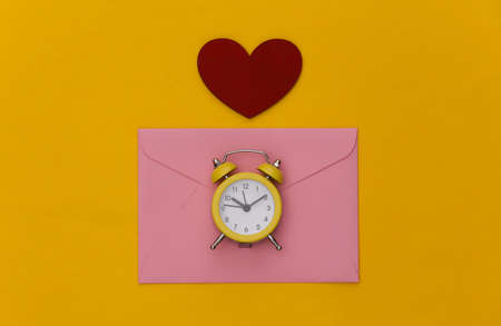 Mini alarm clock and envelopes, heart on yellow background. Happy valentines day. top view. minimalismの写真素材