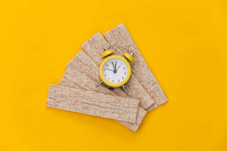 Mini Alarm clock and Diet Crispy Bread on Yellow Background. Diet Time. top viewの写真素材