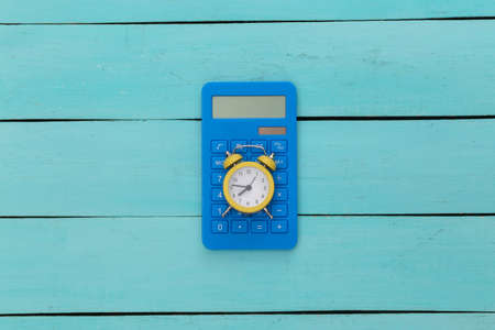 Yellow alarm clock and calculator on blue wooden background. top view.