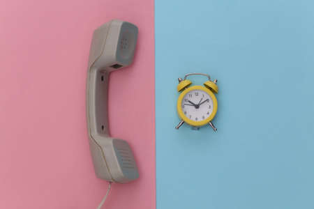 Retro Telephone receiver and alarm clock on pink blue pastel background. top viewの写真素材