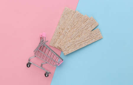 Supermarket Cart with Diet Crispy Bread on Blue Pink Pastel Background. top view