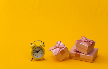Yellow retro alarm clock and gift boxes on yellow background.の写真素材