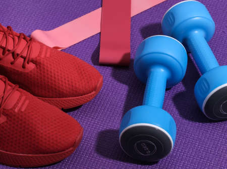Red sports shoes, dumbbells, fitness rubber bands on purple sports mat. Workout concept.の写真素材