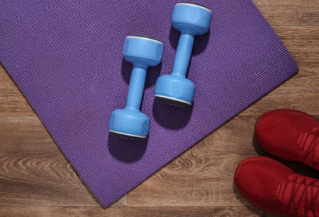 Blue dumbbells, red sport shoes and fitness mat on wooden floor. Workout concept. top viewの写真素材