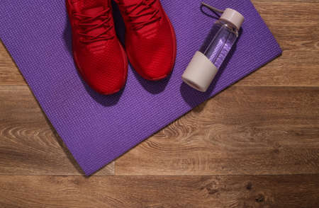 Red sport shoes, water bottle and fitness mat on wooden floor. Workout concept. top viewの写真素材