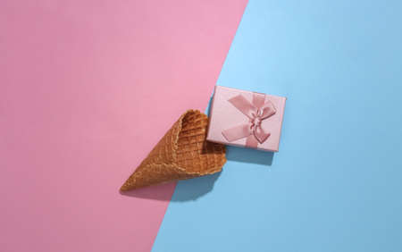 Ice cream waffle cone with gift box on pink and blue bright pastel background with deep shadow, top view. flat lay minimal compositionの写真素材