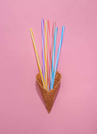 Ice cream waffle cone with cocktail tubes on pink bright pastel background, top view. flat lay...