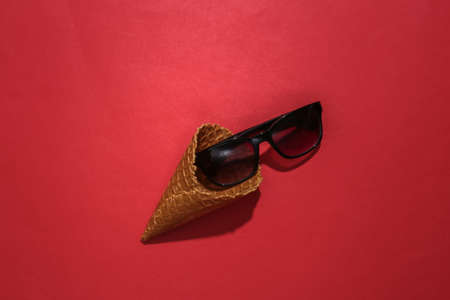 Ice cream waffle cone with sunglasses on red bright background. top viewの写真素材