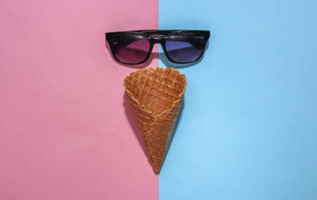 Ice cream waffle cone and sunglasses on pink and blue bright pastel background with deep shadow, top view. Flat lay summer compositionの写真素材