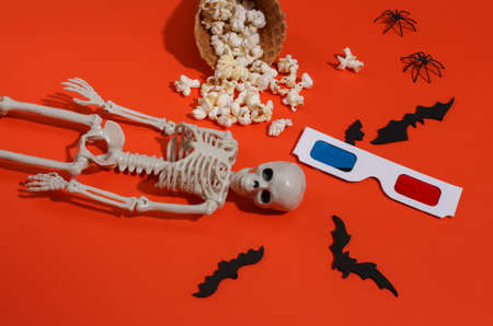 Ice cream waffle cones with popcorn, decorative bats and spiders, skeleton, 3d glasses on orange...