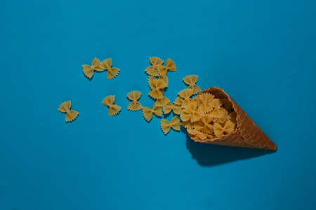Ice cream waffle cone with pasta bows on blue background. top viewの写真素材