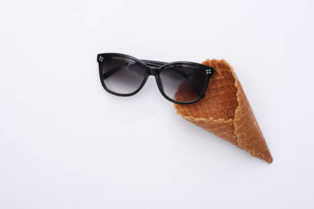 Ice cream waffle cone and sunglasses on white background, top view. Flat lay summer composition