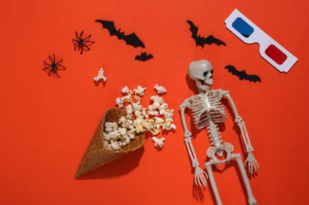 Ice cream waffle cones with popcorn, decorative bats and spiders, skeleton, 3d glasses on orange bright background. top view. scary movie. flat lay halloween compositionの写真素材