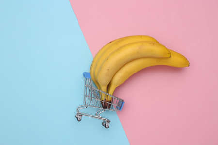 Mini supermarket trolley with ripe bananas on pink blue pastel background. top viewの写真素材