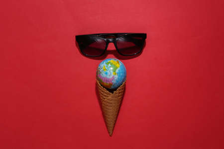 Ice cream waffle cone with globe, sunglasses on red bright background. Summer flat lay. top viewの写真素材