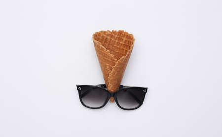 Ice cream waffle cone and sunglasses on white background, top view. Flat lay summer composition
