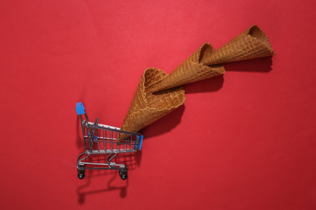 Supermarket trolley with Ice cream waffle cones on red bright background. top view