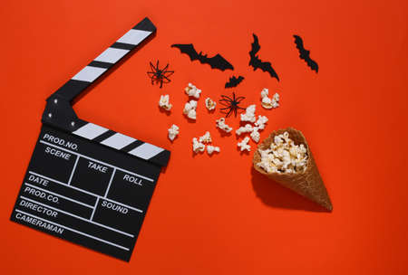 Clapper board, Ice cream waffle cones with decorative bats and spiders, popcorn on orange bright background. top view. scary movie. flat lay halloween compositionの写真素材