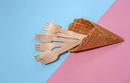 Ice cream waffle cone with wooden forks on pink and blue bright pastel background with deep shadow, top view. flat lay eco compositionの写真素材