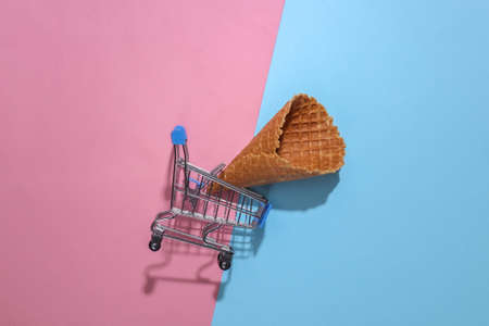 Supermarket trolley with Ice cream waffle cone on pink and blue bright pastel background with deep shadow, top view. flat lay minimal compositionの写真素材